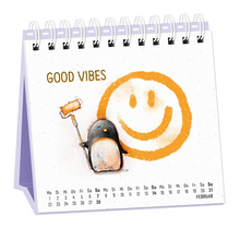 Tischkalender - "Heute. Hier. Jetzt" - 2027 - Monat Februar - Spruch: "Good Vibes" Design: Ein Pinguin, der mit orangener Farbe einen Smiley gemalt hat. Der Hintergrund ist weiß und im Recyclingpapier-Look.