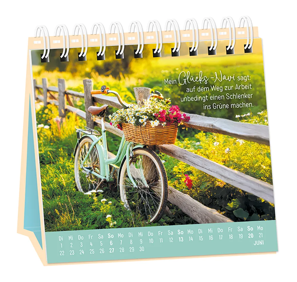 Tischkalender - "Extraportion Glück" - 2027 - Monat Juni - Spruch: "Mein Glücks-Navi sagt: auf dem Weg zur Arbeit unbedingt einen Schlenker ins Grüne machen." Design: Ein Fahrrad mit einem Fahrradkorb voller Blumen angelehnt auf einem Zaun au einer Wiese.
