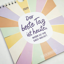 Postkartenkalender - "Der beste Tag" - 2027 - Titelblatt alternative Ansicht - Spruch "Der beste Tag ist heute, wenn du ihn dazu machst." Geschrieben in einer weißen Kreisform aus dem bunte Streifen ausgehen.