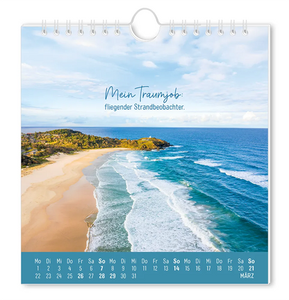Postkartenkalender - "Strandgut" - 2027 - Monat März - Eine schöne Küstenlandschaft mit einer kleinen Siedlung  bei leicht bewölkten Himmel mit dem Spruch "Mein Traumjob: fliegender Strandbeobachter."