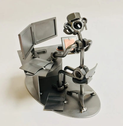 Schraubenfigur Grafikdesigner aus Metall in Rückansicht am Schreibtisch mit zwei Monitoren, Grafiktablett und Bürostuhl