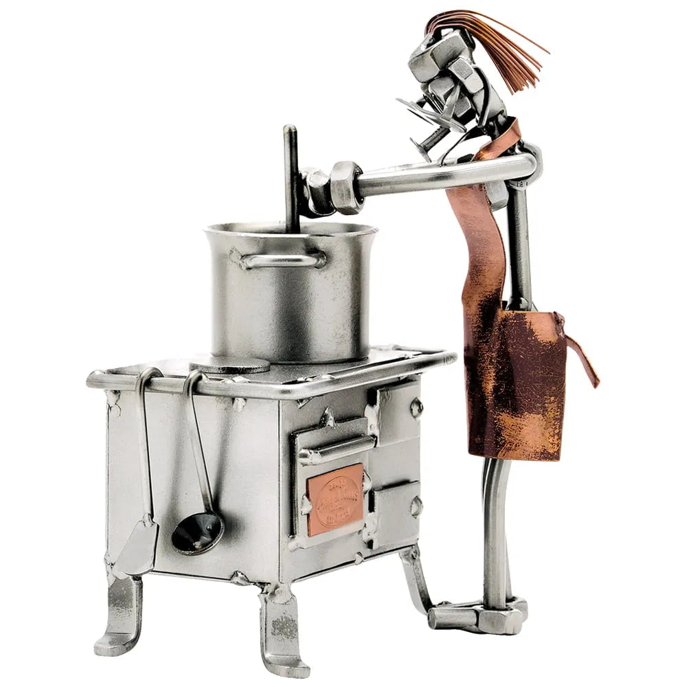 Schraubenfigur einer Köchin mit kupferfarbener Schürze, die in einem Topf auf einem Metallherd rührt.