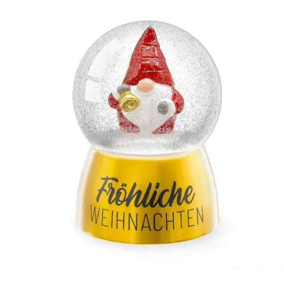 Schneekugel mit Weihnachtswichtel, roter Zipfelmütze und weißem Bart auf goldfarbenem Sockel mit Schriftzug „Fröhliche Weihnachten“