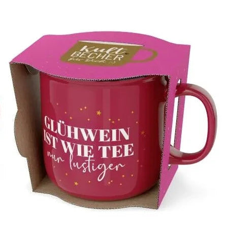 Roter Kultbecher mit goldfarbenen Sternen und Schriftzug „Glühwein ist wie Tee, nur lustiger“ in offener pinkfarbener Geschenkverpackung