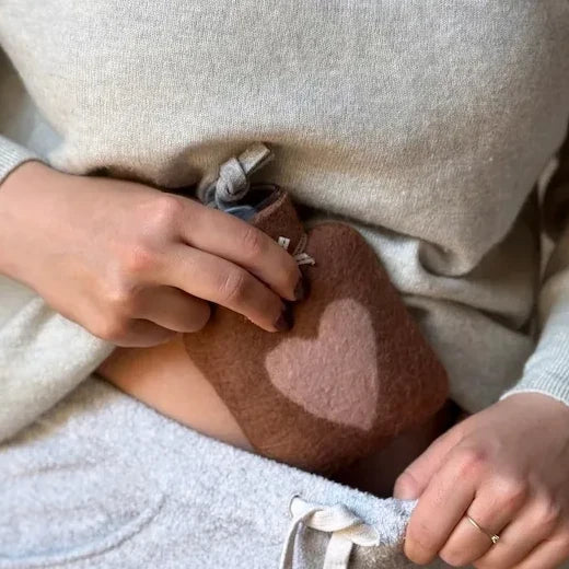 Dorothee Lehnen Wärmflasche mit braunem Merinowollbezug und rosa Herz als hochwertiges Geburtstagsgeschenk, am Bauch gehalten