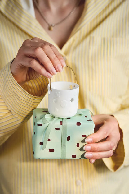 Räder Geschenklaterne „Denk an dich“ aus weißem Porzellan mit Blumenmotiv auf einem mintgrün verpackten Geschenk, am goldfarbenen Henkel gehalten