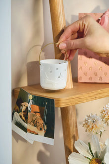 Räder Geschenklaterne „Time to be happy“ aus weißem Porzellan mit Hundemotiv und Musiknoten, am goldfarbenen Henkel über einem Holzregal gehalten