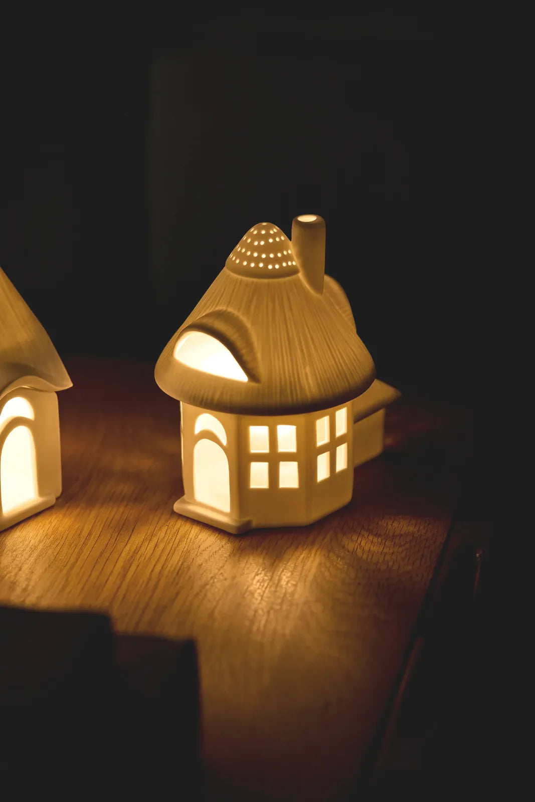 Warm beleuchtetes räder Lichthaus „Reetdachturm“ aus Porzellan mit leuchtenden Fenstern, Dachgaube und Lichtpunkten im Turmdach auf einem Holztisch